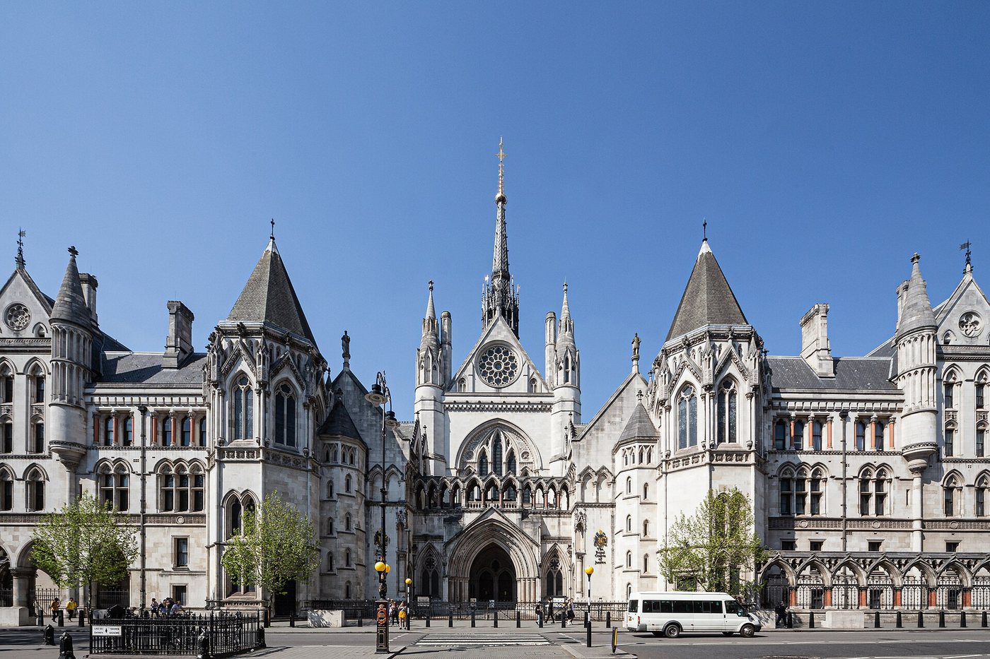 The Gothic Revival main entrance of the Royal Courts of Justice on the Strand, London, under a clear blue sky.