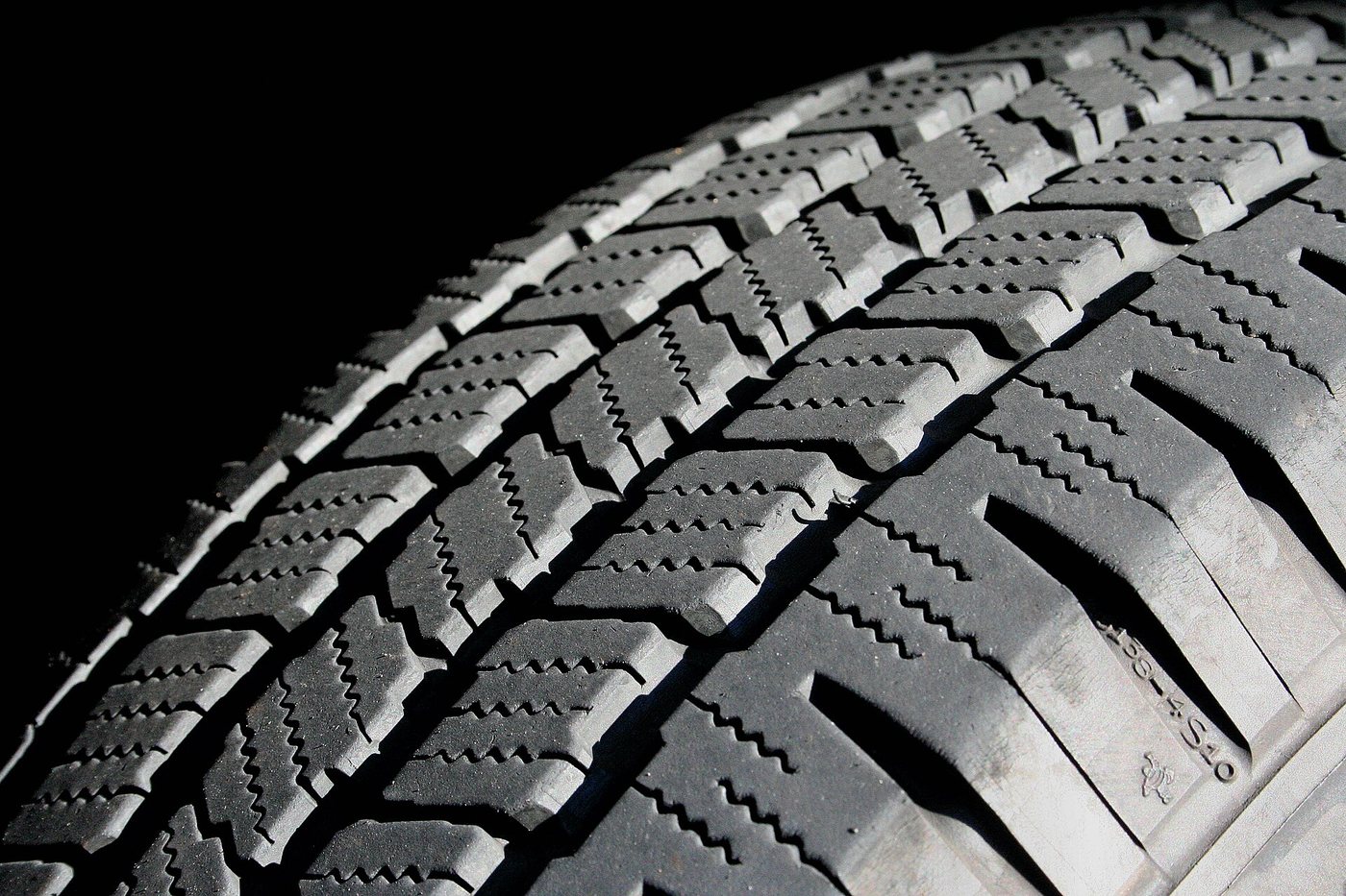 Close-up of the siped tread blocks of a car tyre against a black background.